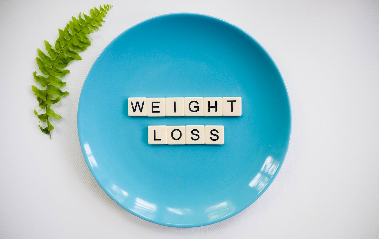 services-03 A blue plate with 'weight loss' tiles and a fern leaf on white background.